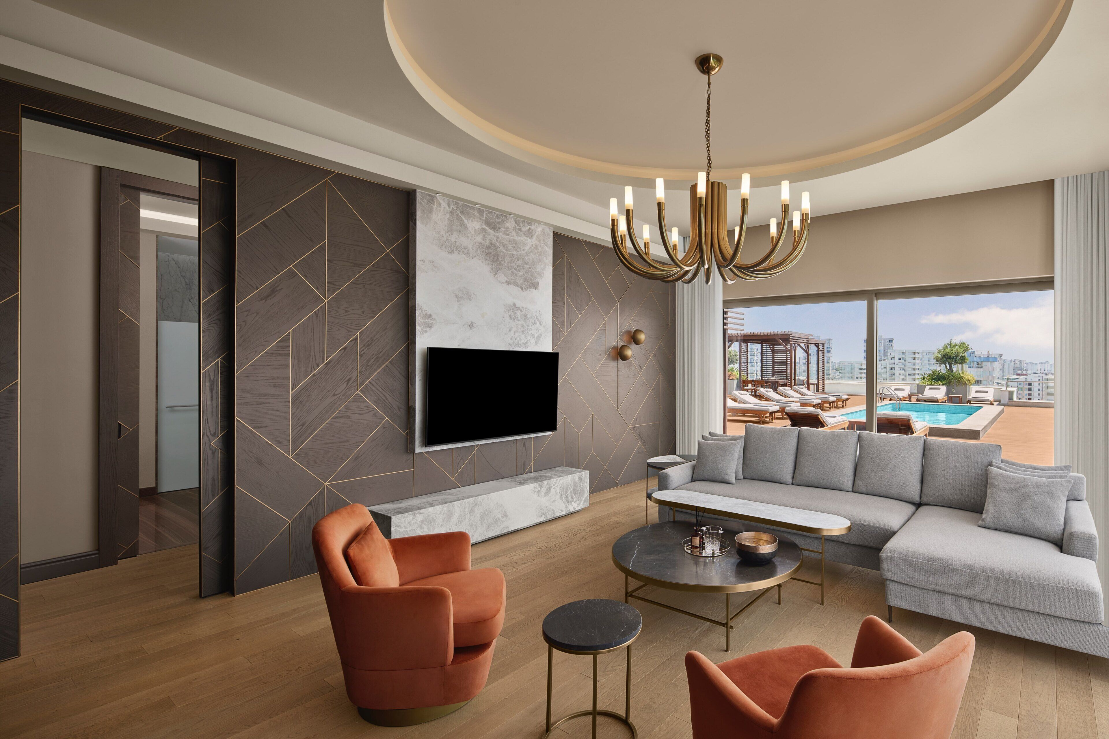A modern living room with a large flat-screen TV, a grey sectional sofa, and orange armchairs.