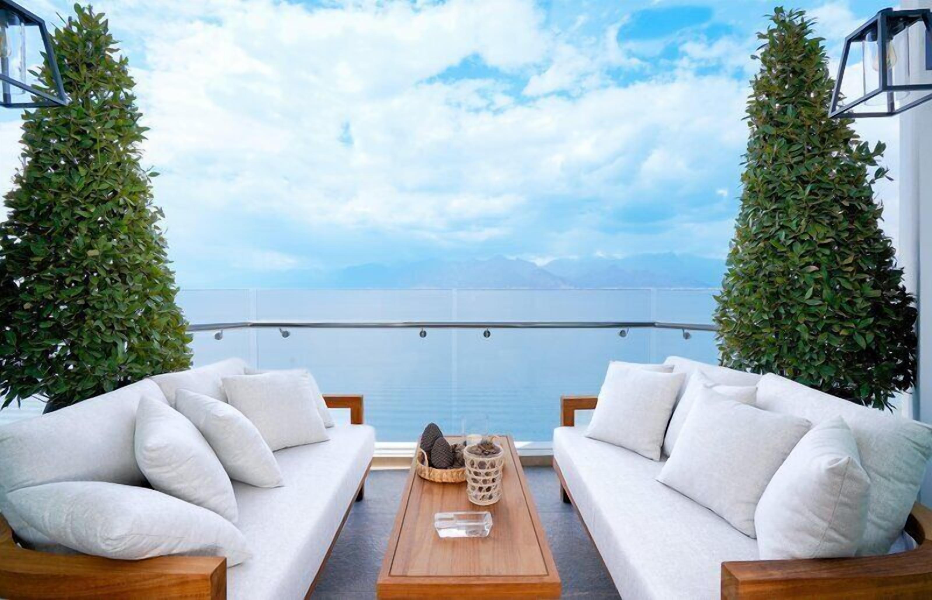 A balcony with two white sofas, a wooden coffee table, and a view of the sea.