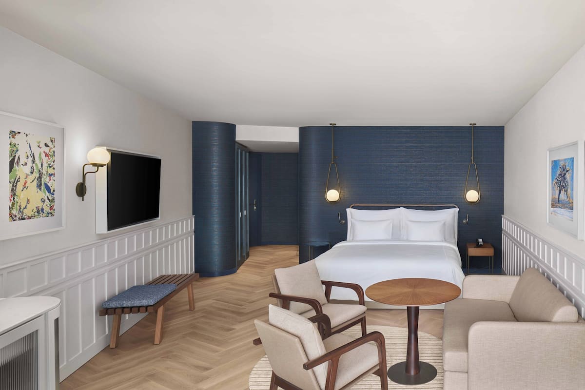 A modern hotel room with a large bed, a seating area with a table, and a TV mounted on the wall.