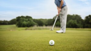 Een golfbal op een green, met een golfclub in beweging.