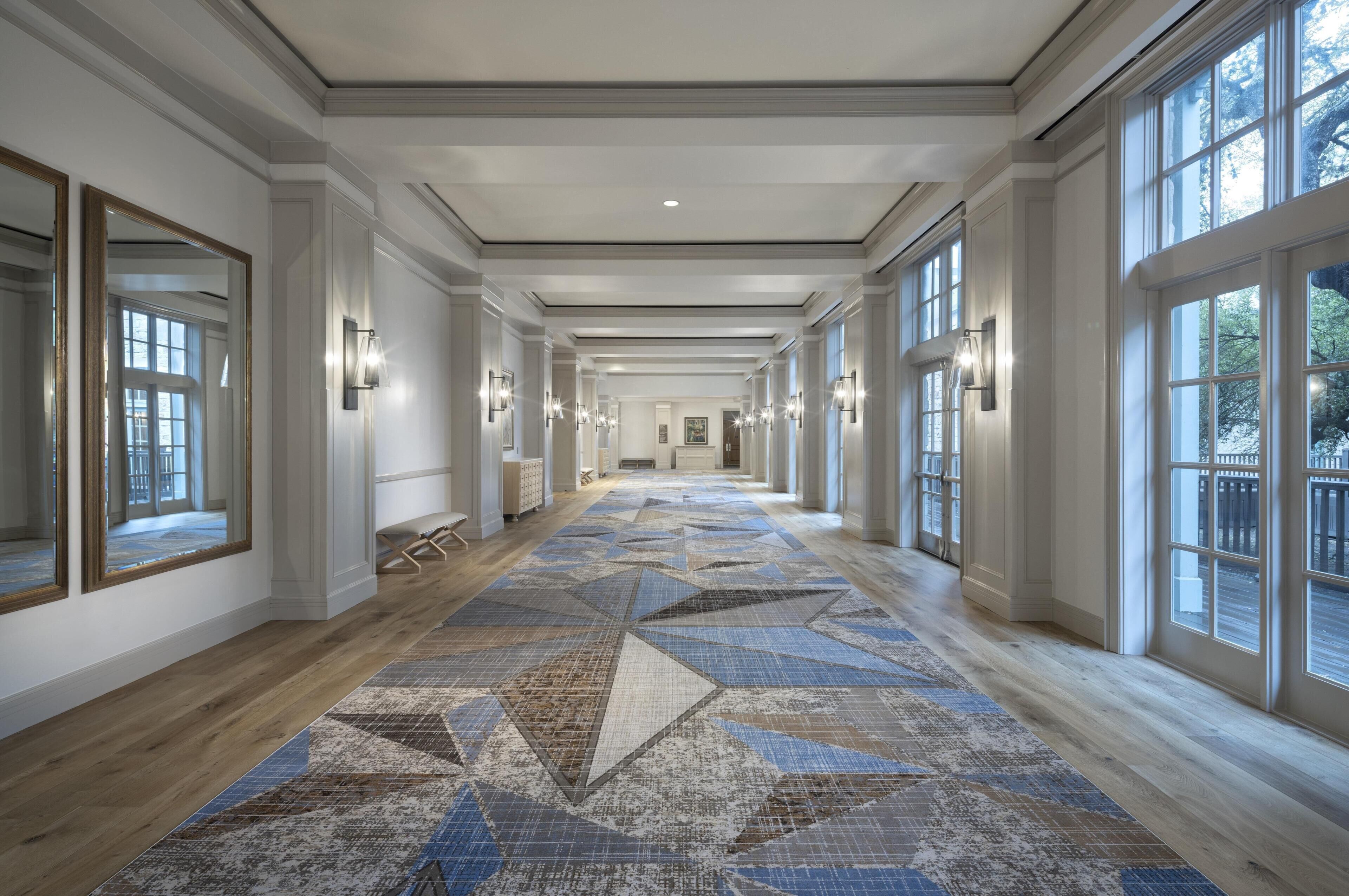 Un long couloir bien éclairé, doté de grandes fenêtres, d’un tapis à motifs et d’appliques murales.