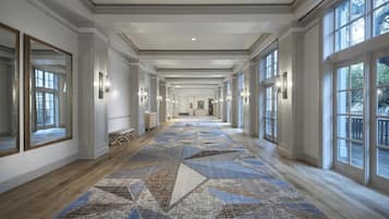 A long, well-lit hallway with large windows, a patterned carpet, and wall sconces.