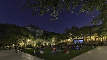 An outdoor seating area with a large screen for movie viewing, surrounded by trees and buildings.