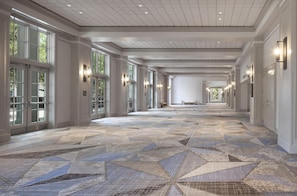 A long corridor with patterned flooring, large windows, and wall sconces.