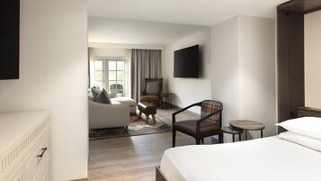 A hotel room with a bed, a sofa, a chair, a small table, a TV, and a window with curtains.