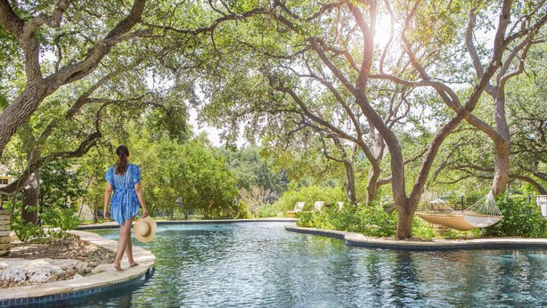A pool area with a person standing on a platform, surrounded by trees and a hammock. - Hyatt Regency Hill Country Resort and Villas (San Antonio)