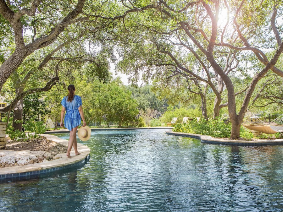 A pool area with a person standing on a platform, surrounded by trees and a hammock.