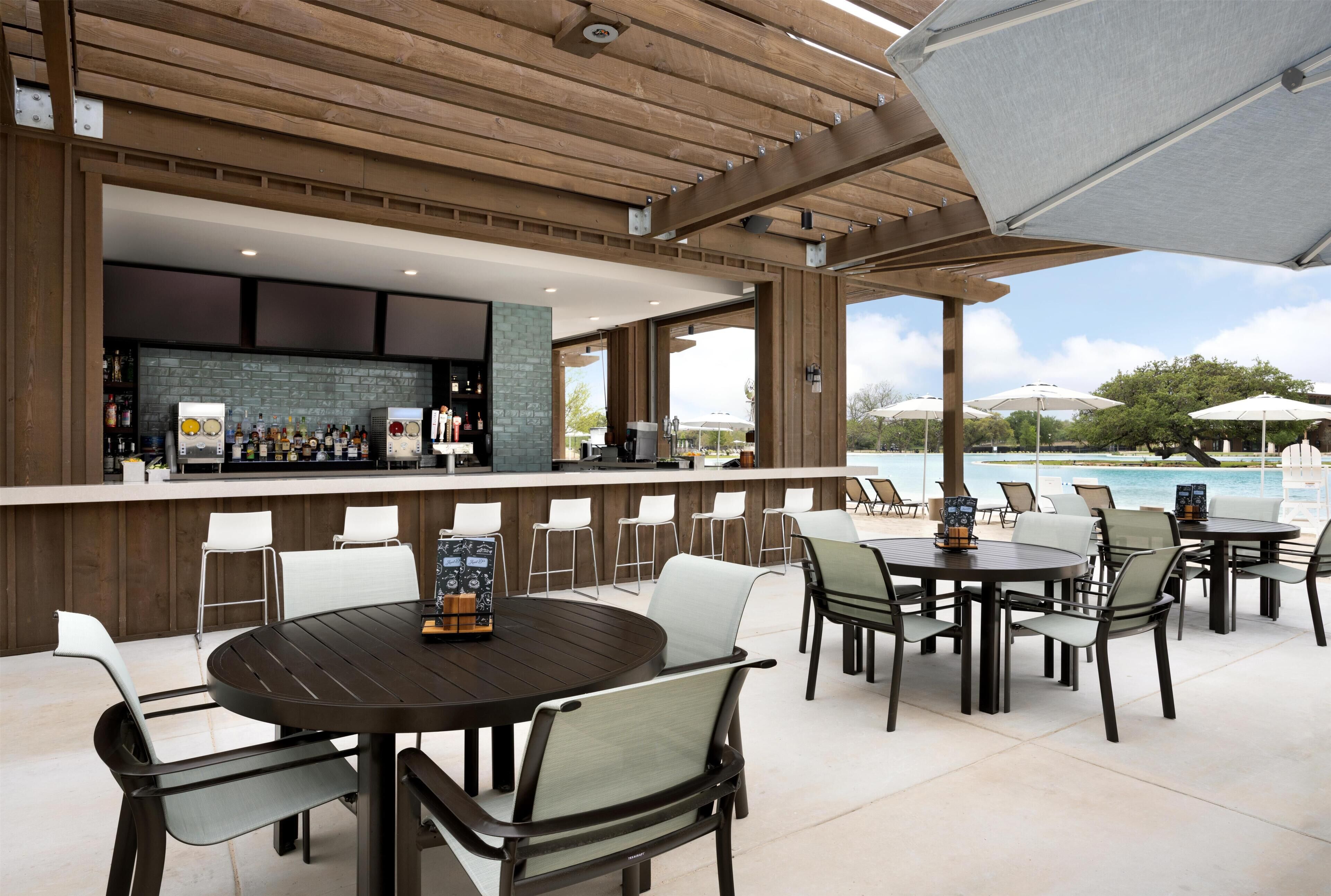 An outdoor bar area with a pool view, wooden ceiling, and multiple seating arrangements.