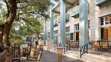 Un edificio con terraza al aire libre, paredes de piedra y un árbol grande.