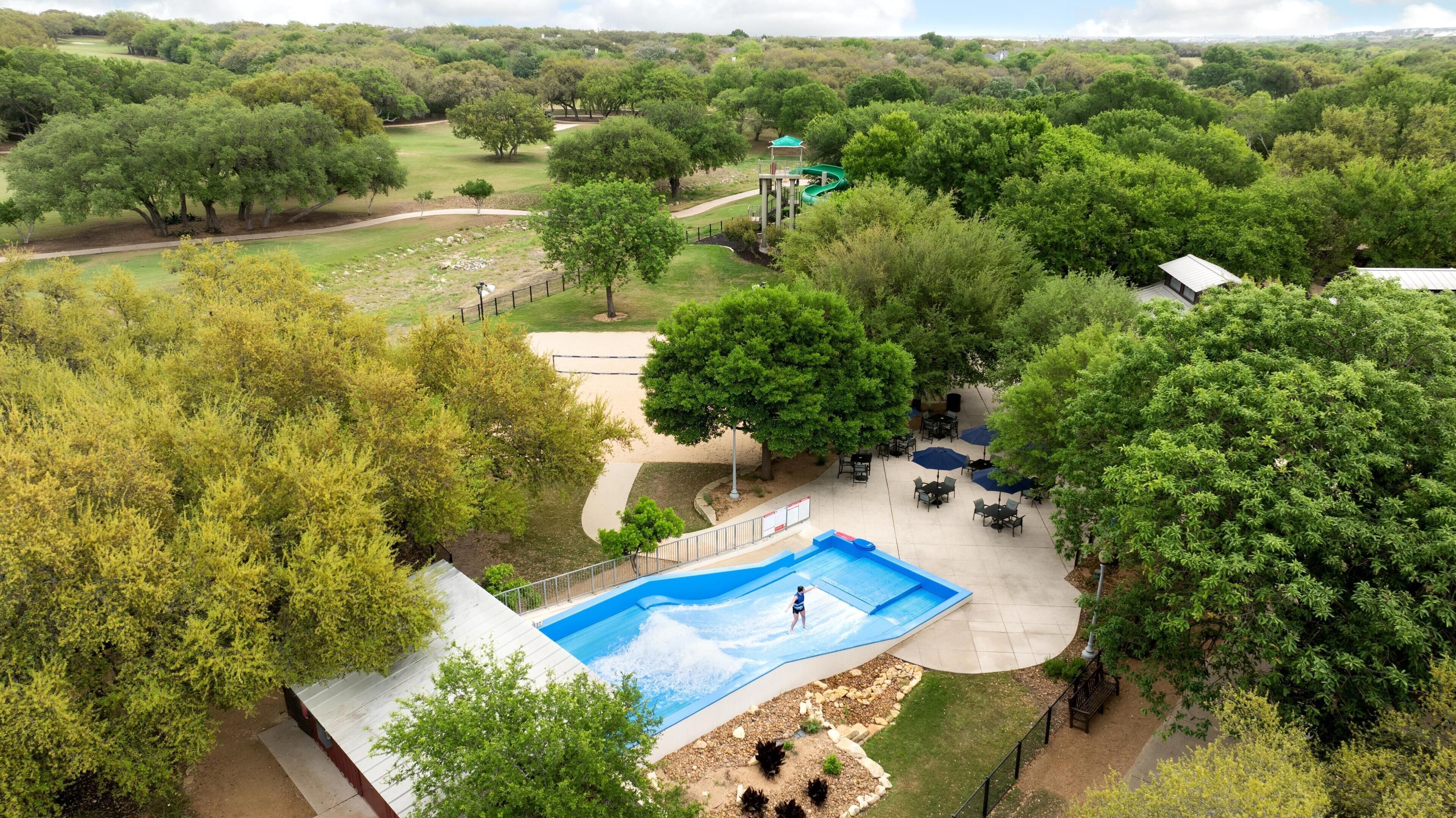 An aerial view of a property with a swimming pool, outdoor seating, and a golf course in the background.