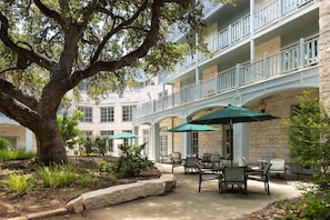 A courtyard with outdoor seating, a large tree, and a multi-story building with balconies.