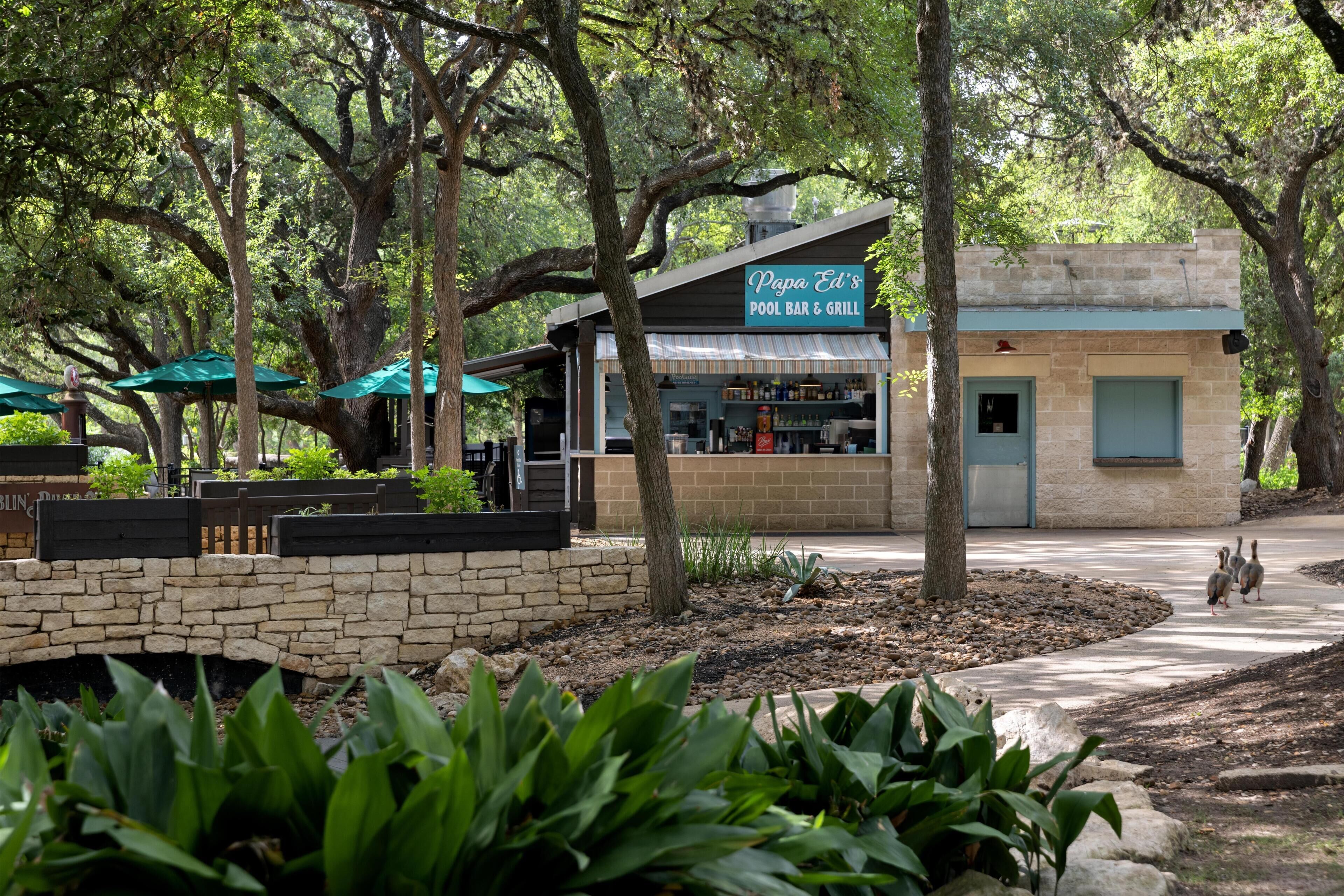 A small building labeled 'Papa Ed's Pool Bar & Grill' with outdoor seating and a stone wall.