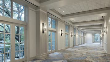 A long corridor with large windows, a patterned floor, and wall sconces.