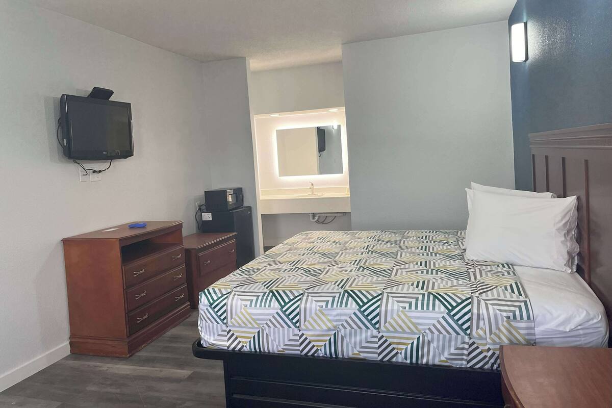 A bedroom with a bed, dresser, TV, and a mirror.