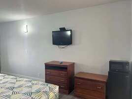 Un dormitorio con cama, cómoda, televisor montado en la pared y refrigerador.