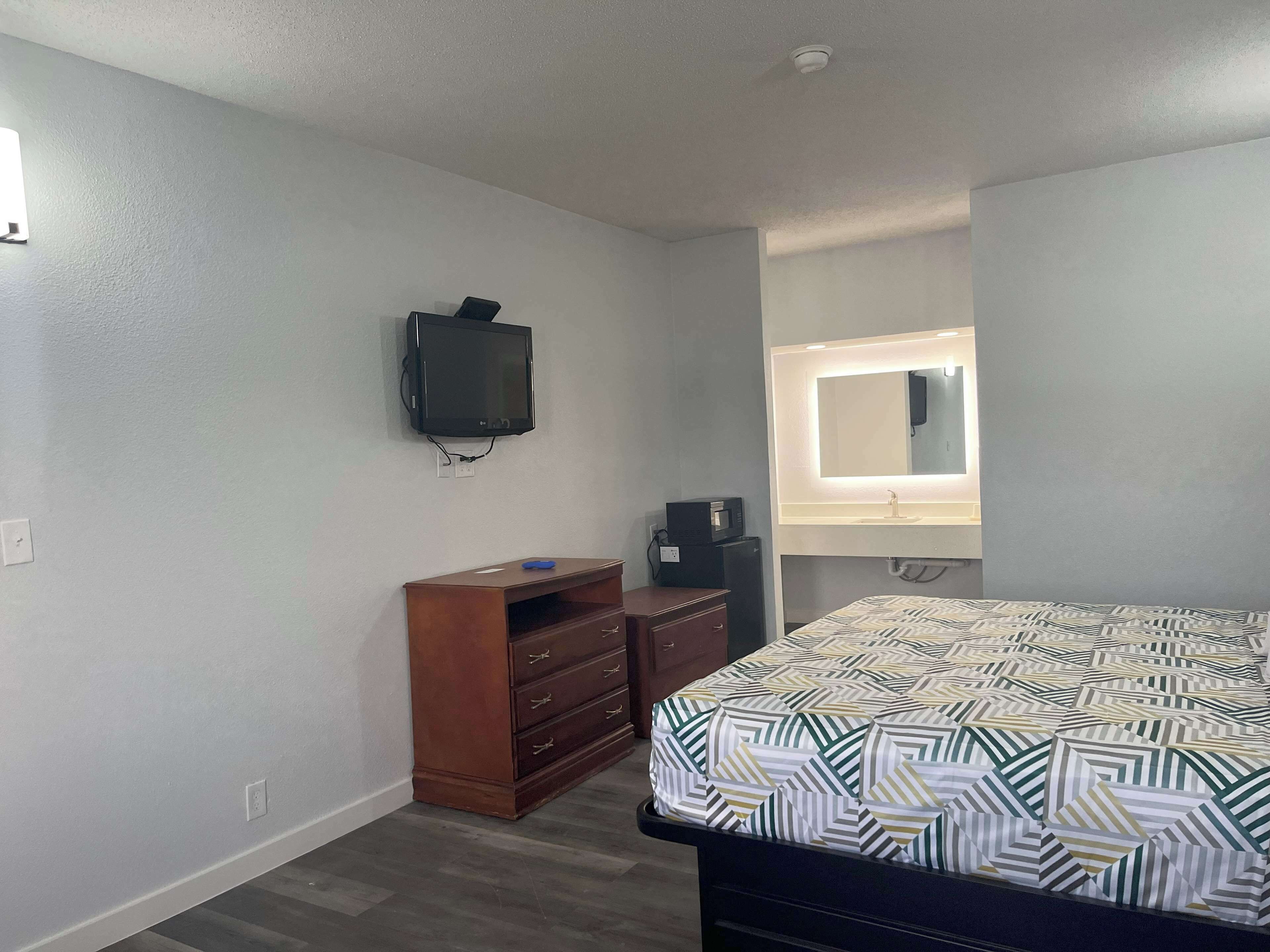 Un dormitorio con cama, cómoda, televisor y espejo con iluminación.