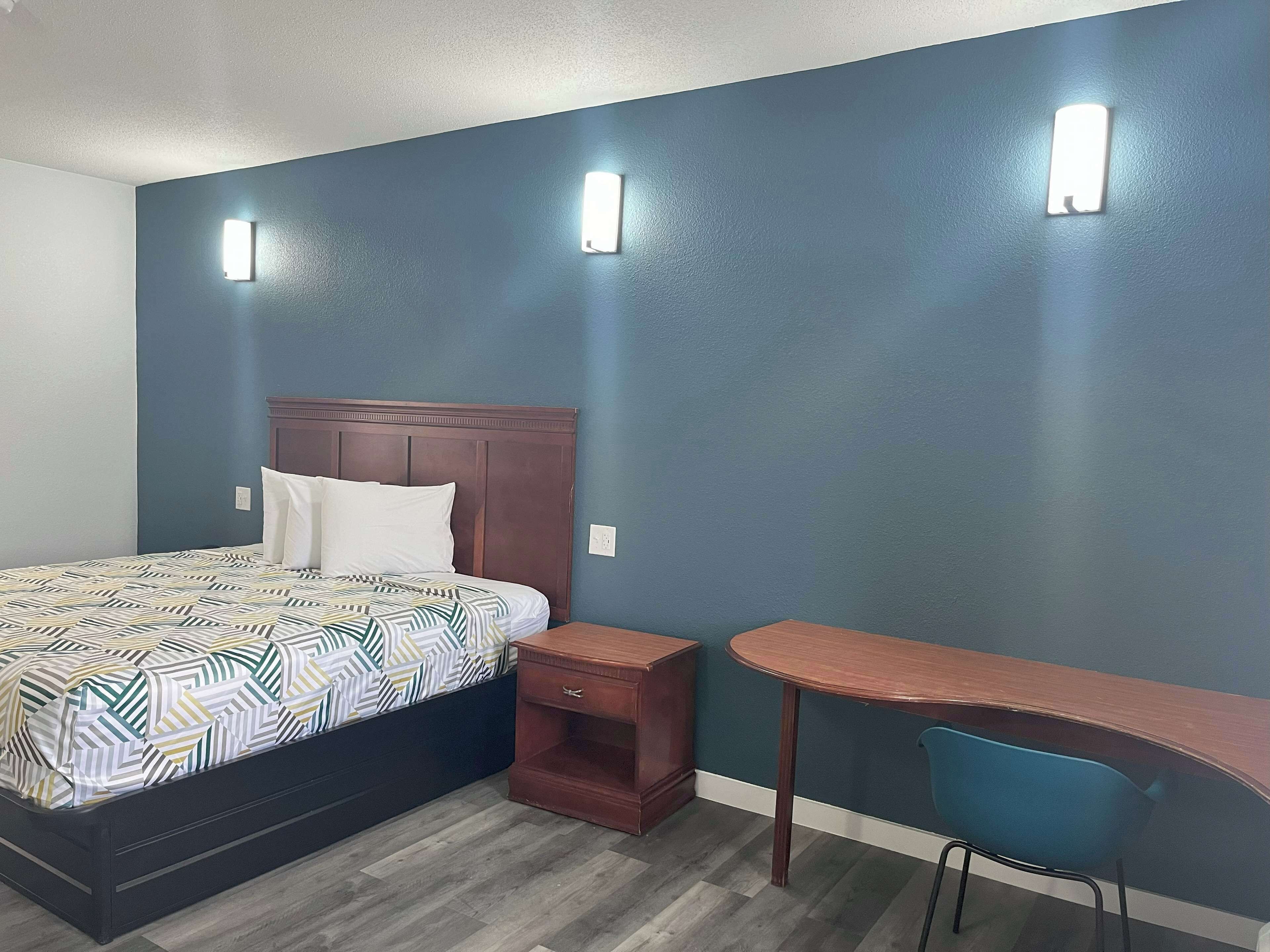 A bedroom with a bed, bedside table, and desk with chair.
