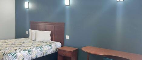 A bedroom with a bed, bedside table, and desk with chair.