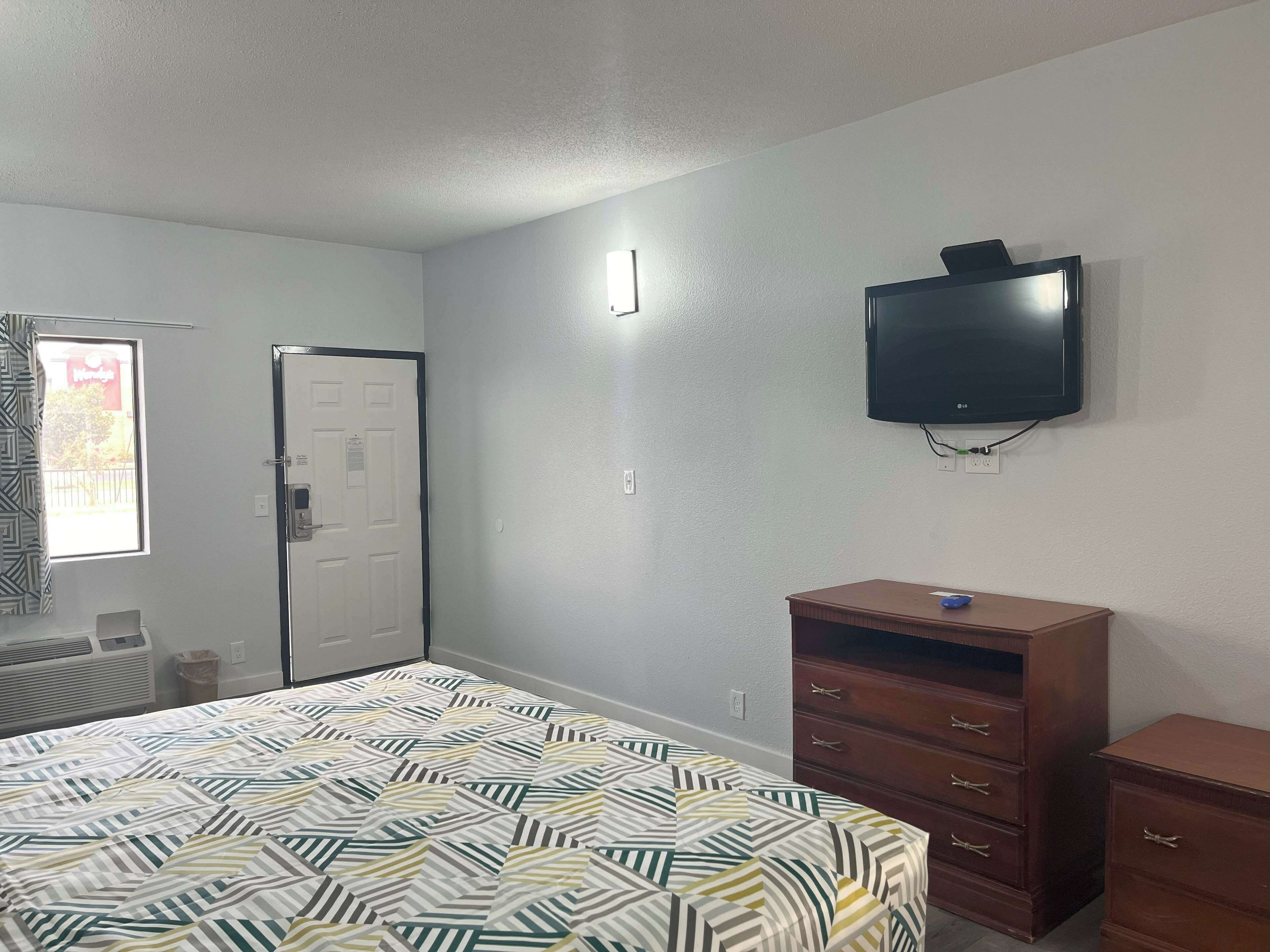Une chambre à coucher avec un lit, une commode, un téléviseur et une porte.