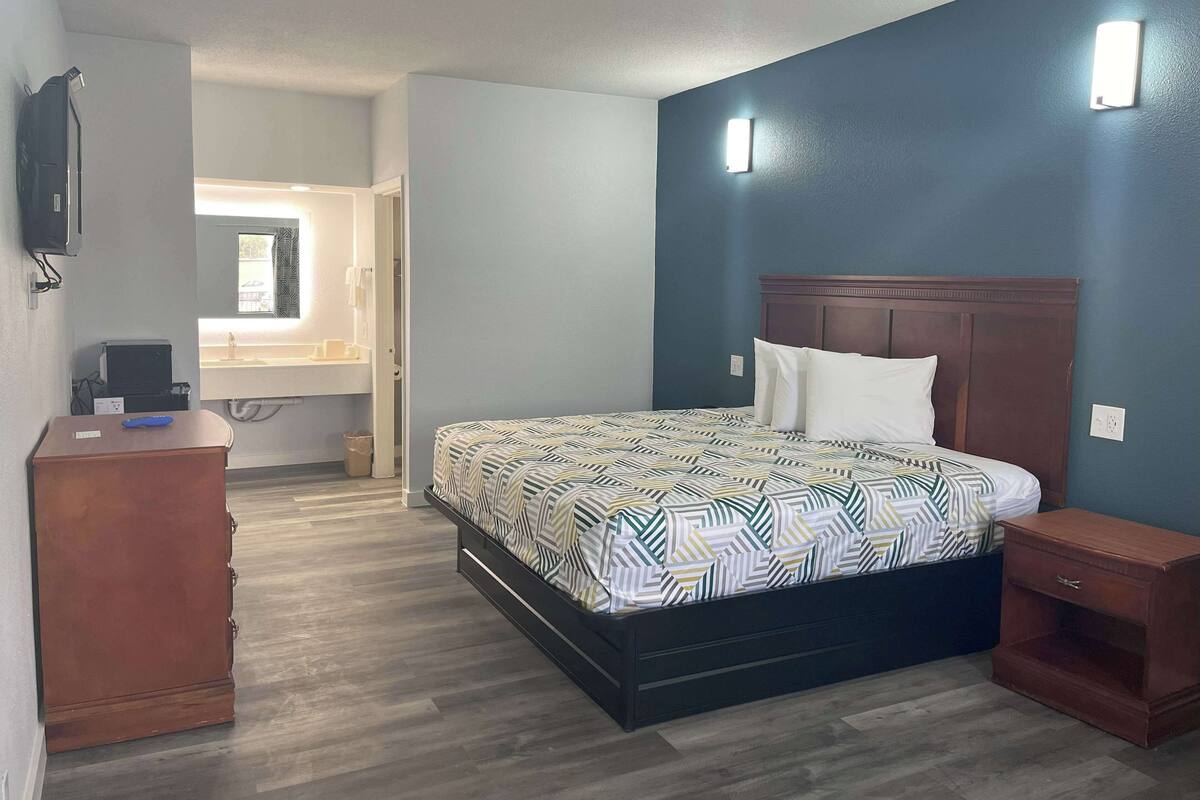 A bedroom with a bed, a nightstand, a dresser, and a wall-mounted TV.