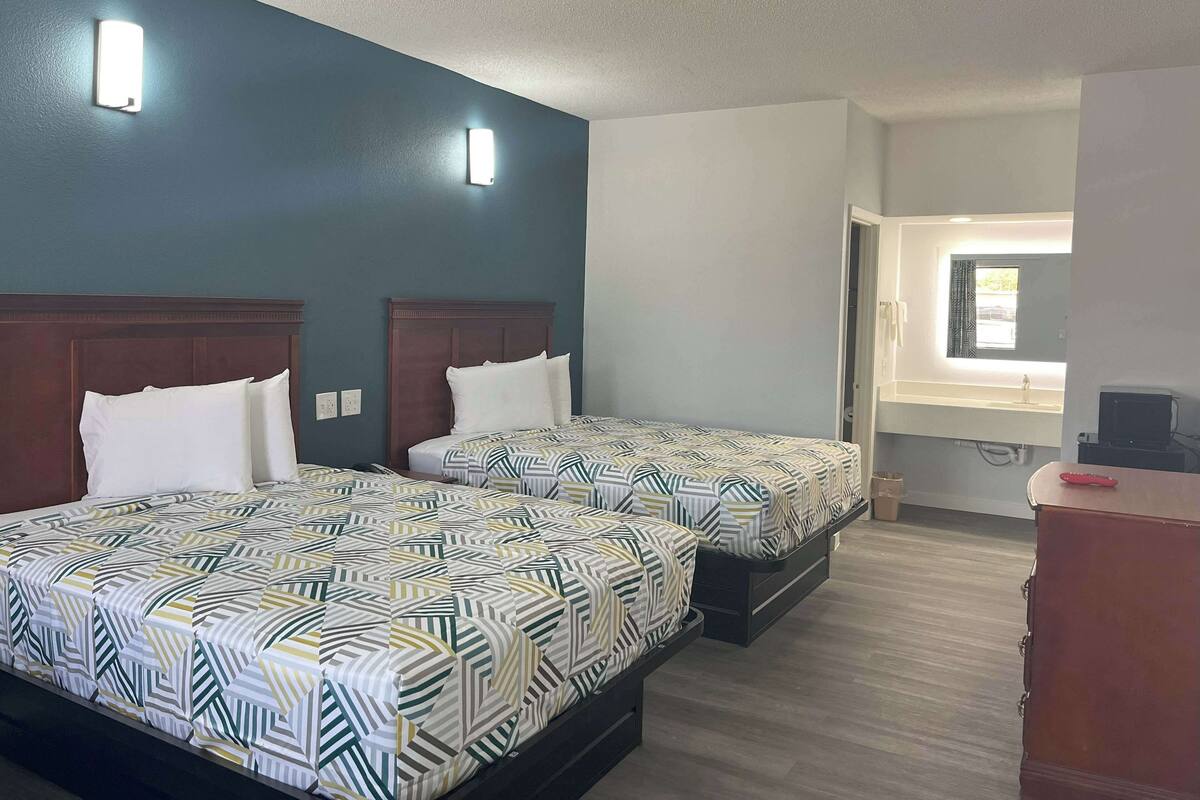 A hotel room with two beds, a wooden headboard, a window with a view, and a desk with a computer.