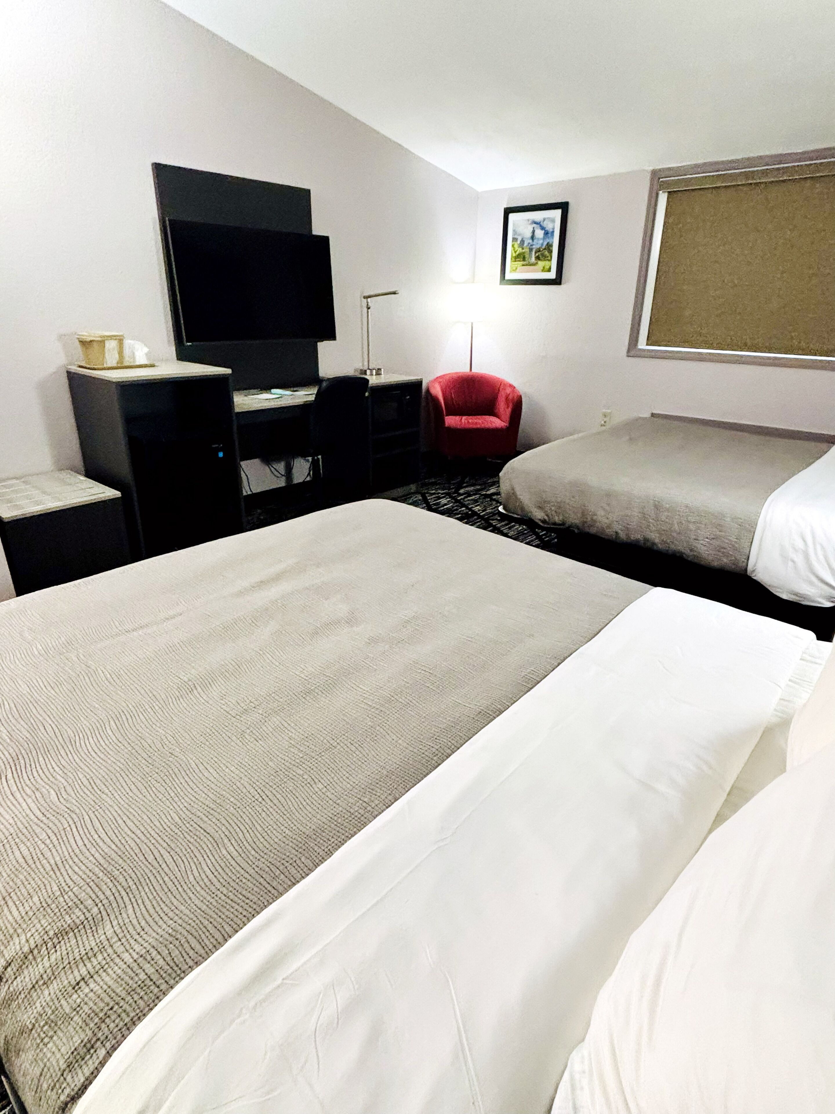A hotel room with two beds, a desk with a computer, a red chair, and a television.