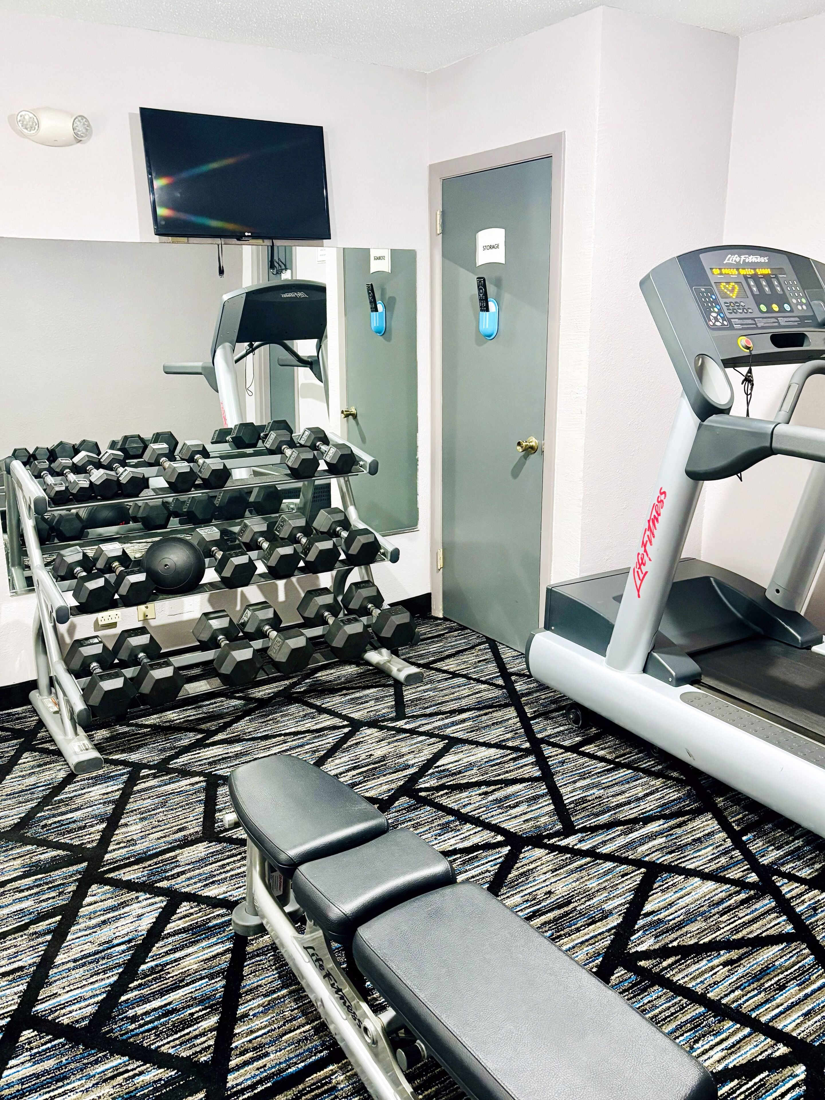 Une salle de sport équipée de matériel d’exercice, notamment des haltères, un tapis de course et un banc.