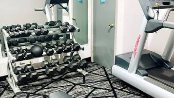 Une salle de sport équipée de matériel d’exercice, notamment des haltères, un tapis de course et un banc.