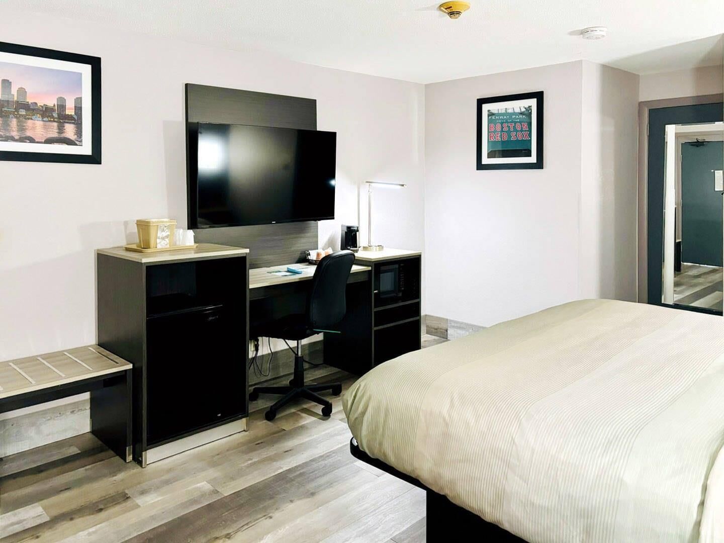 Une chambre d’hôtel avec un lit, un bureau équipé d’un ordinateur, un téléviseur à écran plat et un tableau représentant le stade de Fenway Park.