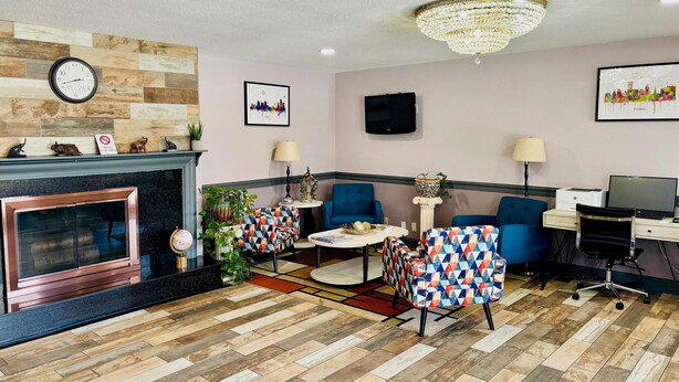 A hotel room with a fireplace, two blue armchairs, a round table, a TV, and a desk with a computer. - Quality Inn Raynham - Taunton (Raynham)