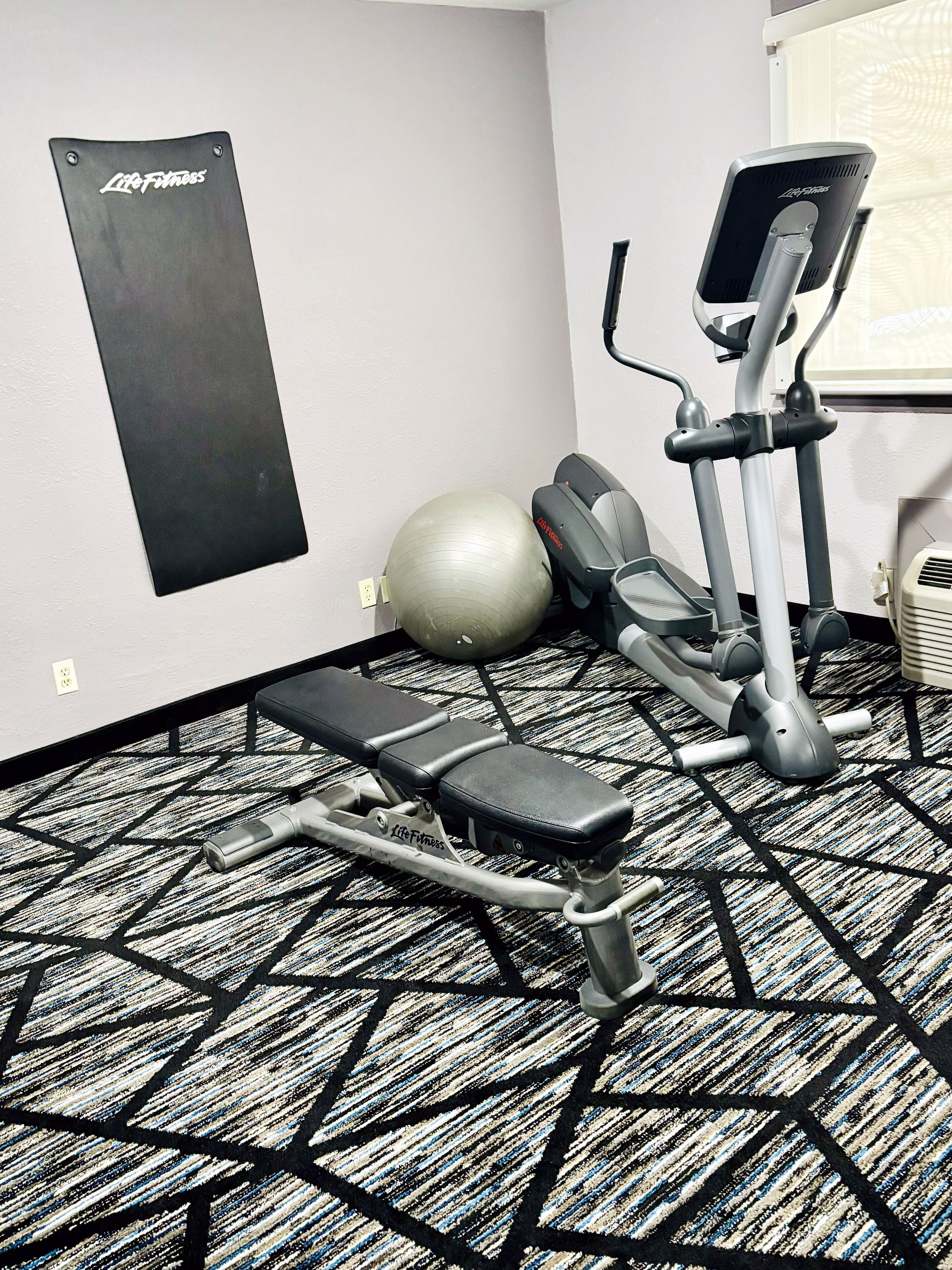Gimnasio con una plataforma elevada, elíptica y una pelota de ejercicios grande.