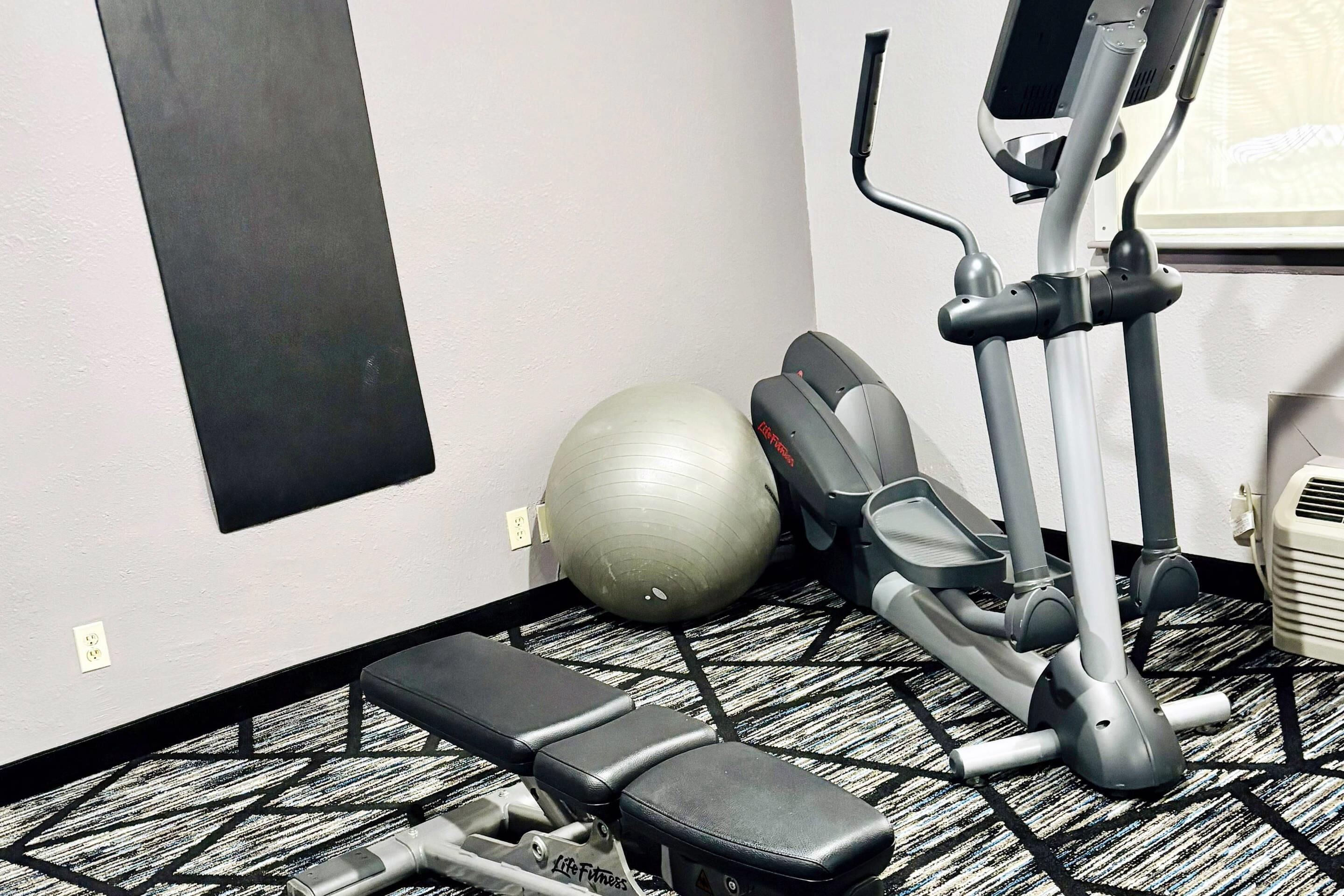 Une salle de sport équipée de divers appareils, notamment un tapis de course, un vélo elliptique et un vélo d’appartement.