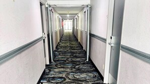 A hotel hallway with a patterned carpet, doors on both sides, and a light-colored ceiling. - Quality Inn Raynham - Taunton (Raynham)
