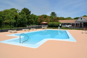 A swimming pool with lounge chairs and a covered area, surrounded by a fence and trees.