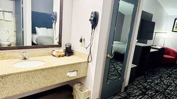 A hotel bathroom with a sink, mirror, hairdryer, and a trash bin.