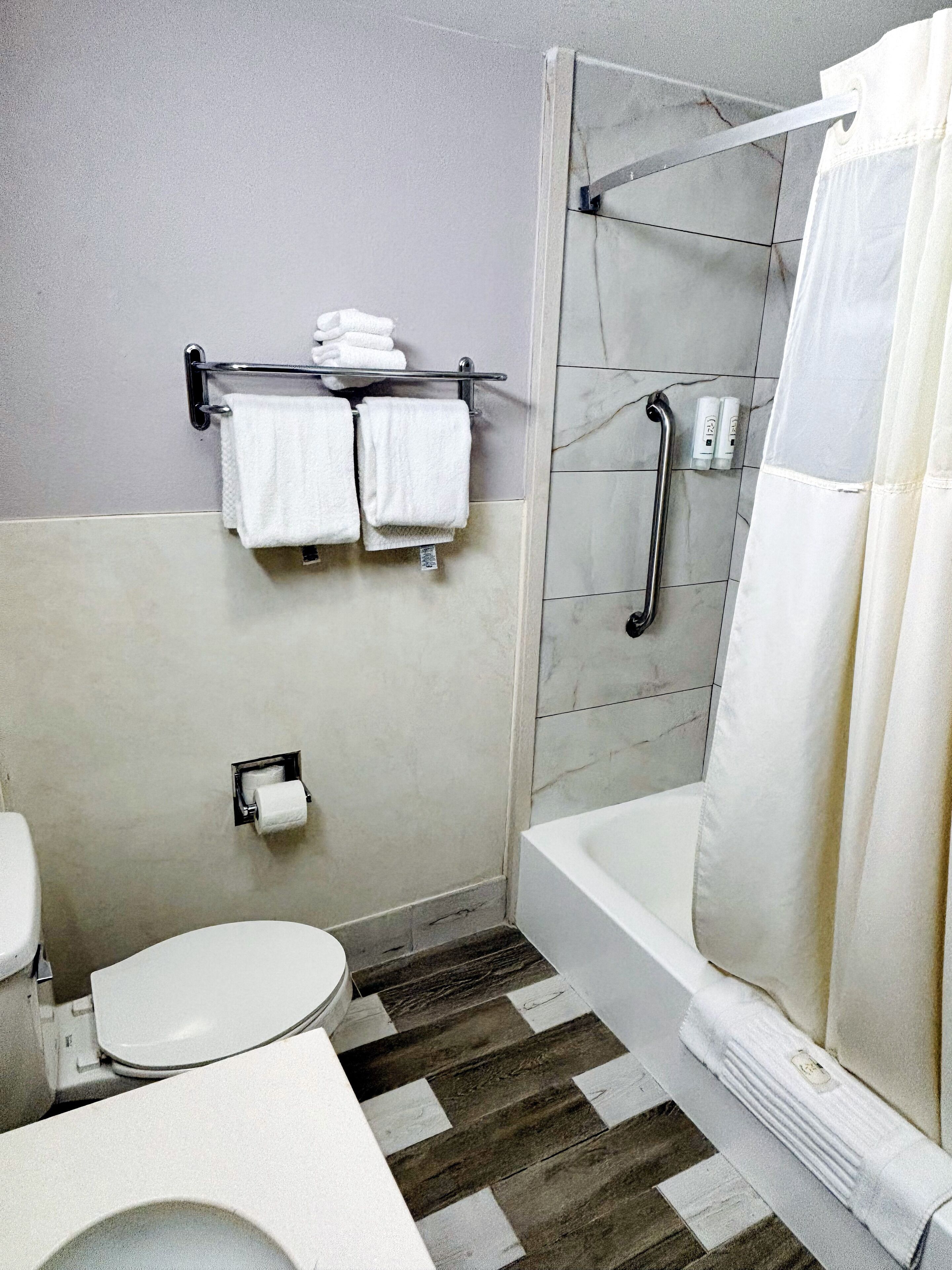 A bathroom with a toilet, a shower with a glass door, a towel rack with towels, and a toilet paper holder.