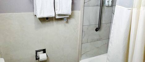A bathroom with a toilet, a shower with a glass door, a towel rack with towels, and a toilet paper holder.
