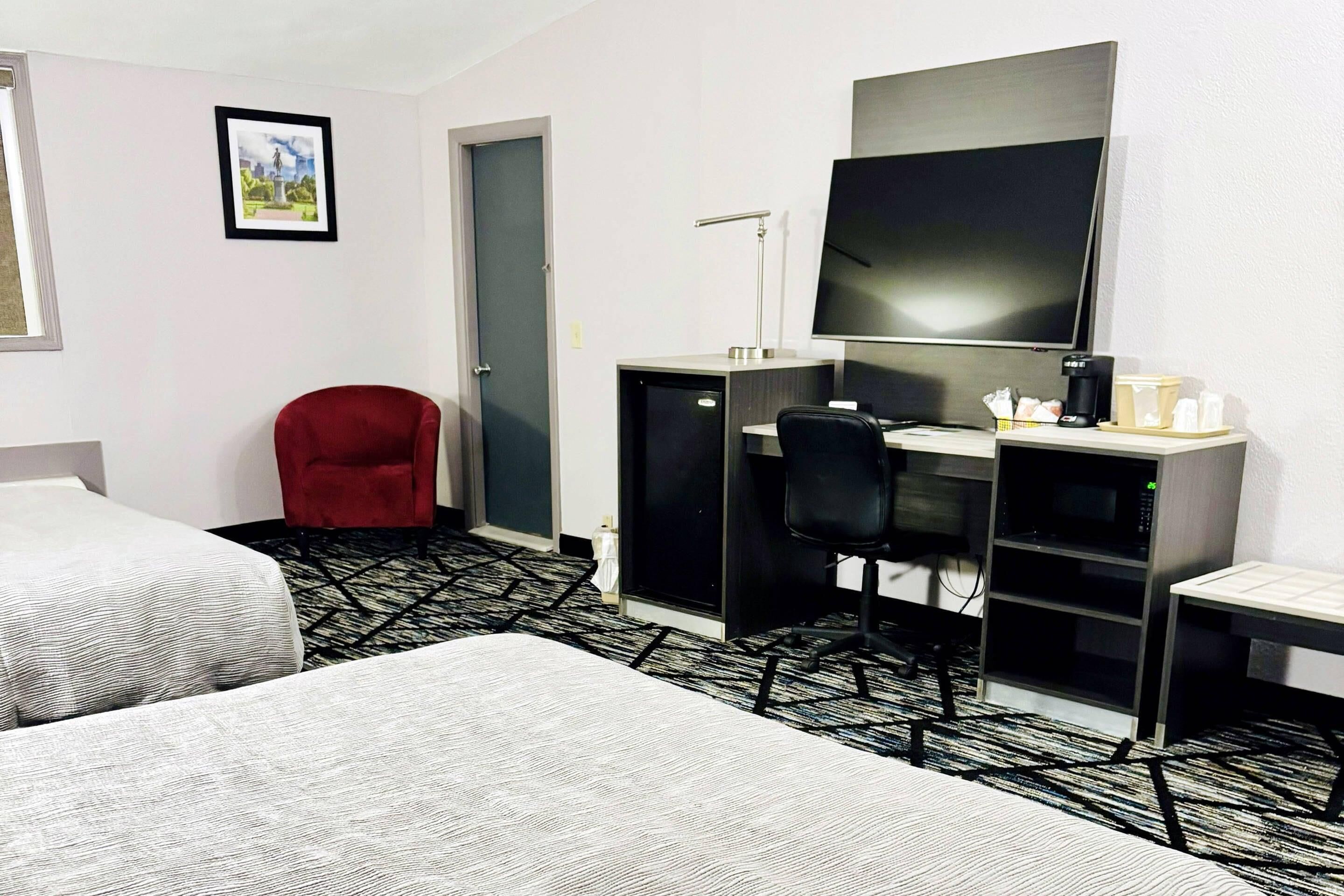 Een hotelkamer met twee bedden, een bureau met een computer, een televisie en een rode stoel.