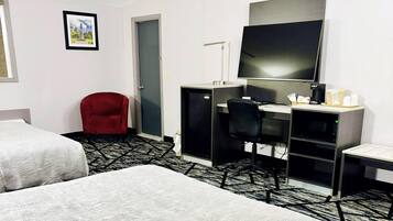 Een hotelkamer met twee bedden, een bureau met een computer, een televisie en een rode stoel.