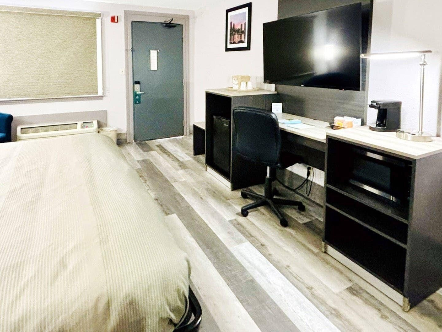Habitació d'hotel amb llit, escriptori amb ordinador, cadira, televisió i porta.