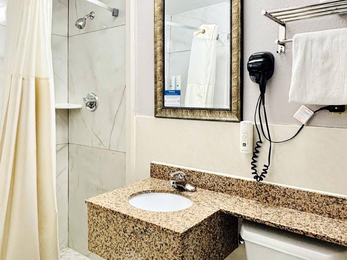 Une salle de bain équipée d’un lavabo en granit, d’un miroir, d’un sèche-cheveux et d’un porte-serviettes.