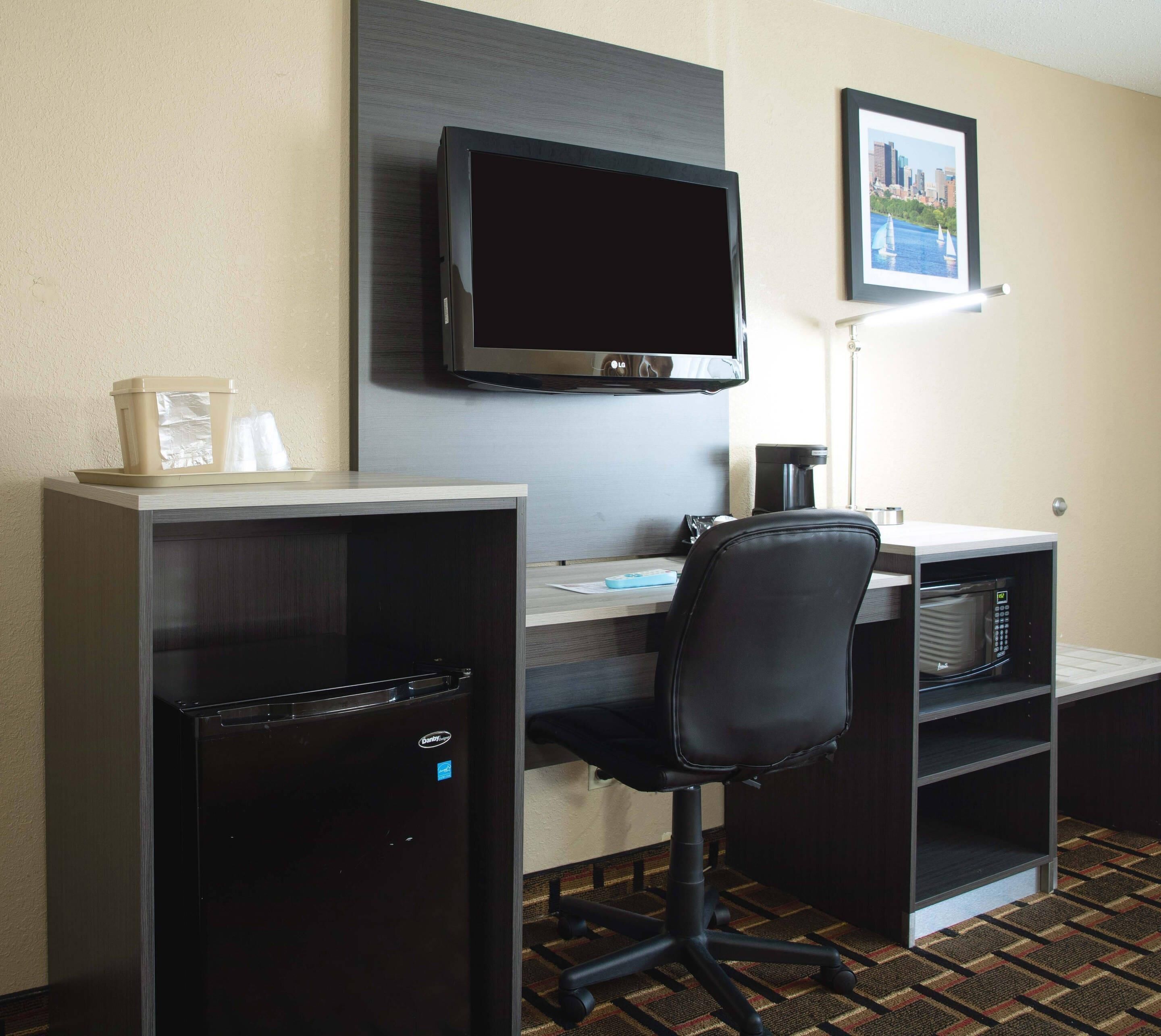 A hotel room with a flat-screen TV mounted on the wall, a desk with a chair, a minibar, and a microwave.