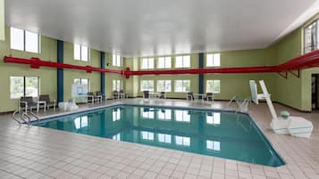 An indoor swimming pool with clear blue water, tiled floor, and a red pipe running across the ceiling.