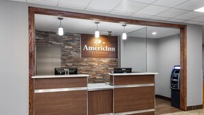 Un espace d’accueil avec un comptoir de réception en bois, un ordinateur Dell et un distributeur automatique de billets.