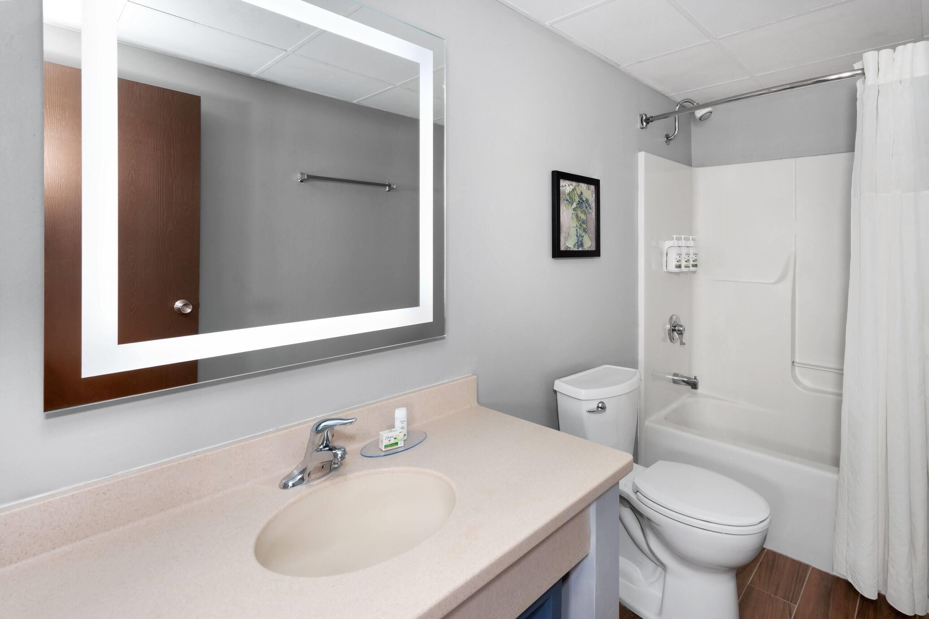 A modern bathroom with a large mirror, a sink, a toilet, and a bathtub.
