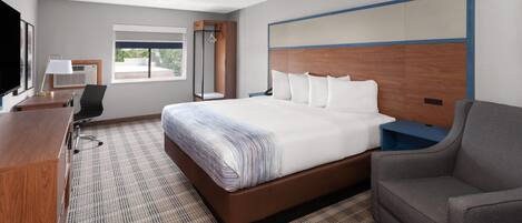 A hotel room with a large bed, a desk, a chair, a TV, and a window.