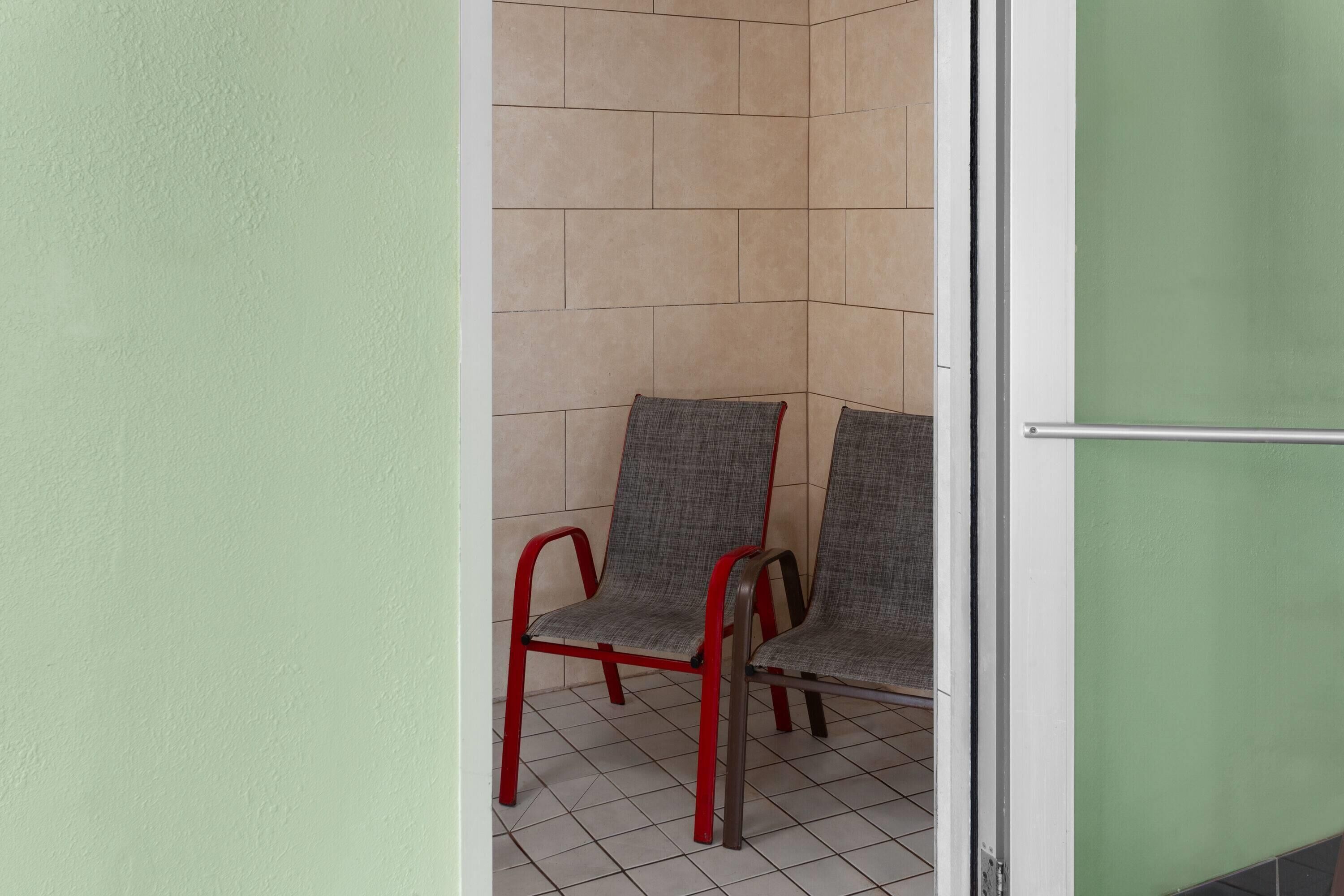 Esquina de una habitación con dos sillas, piso de baldosas y pared verde.
