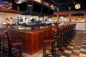 A bar area with a checkered floor, wooden bar counter, and multiple bar stools. - AmericInn & Suites By Wyndham Baraboo Event Center (Baraboo)