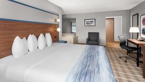 Une chambre d’hôtel avec un grand lit, un bureau, une chaise, une salle de bain et un tableau encadré au mur.