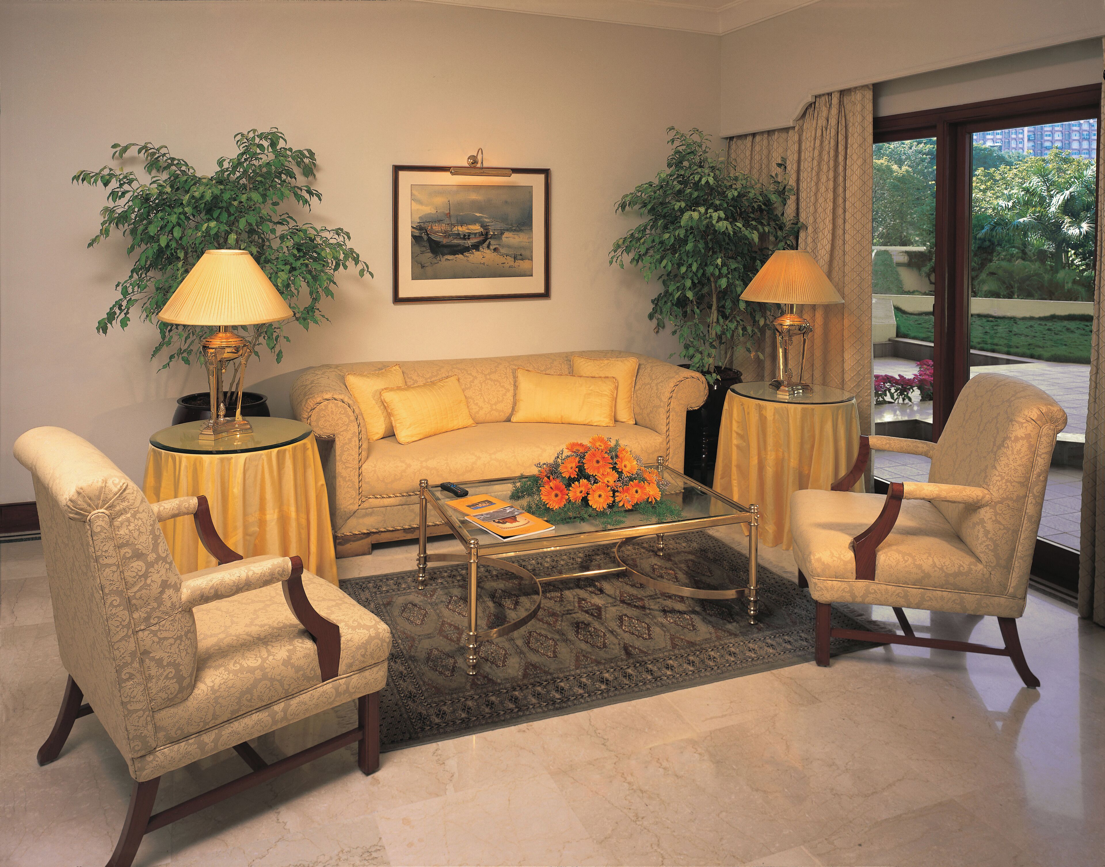 A living room with a sofa, two armchairs, a coffee table, and two lamps. There is a painting on the wall and a window with curtains.